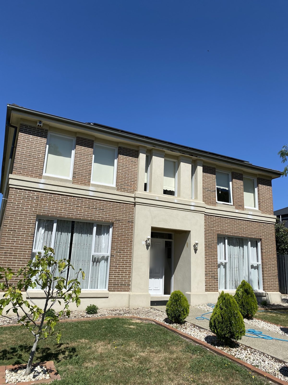 Double-storey brick home with freshly painted cream render bands and portico