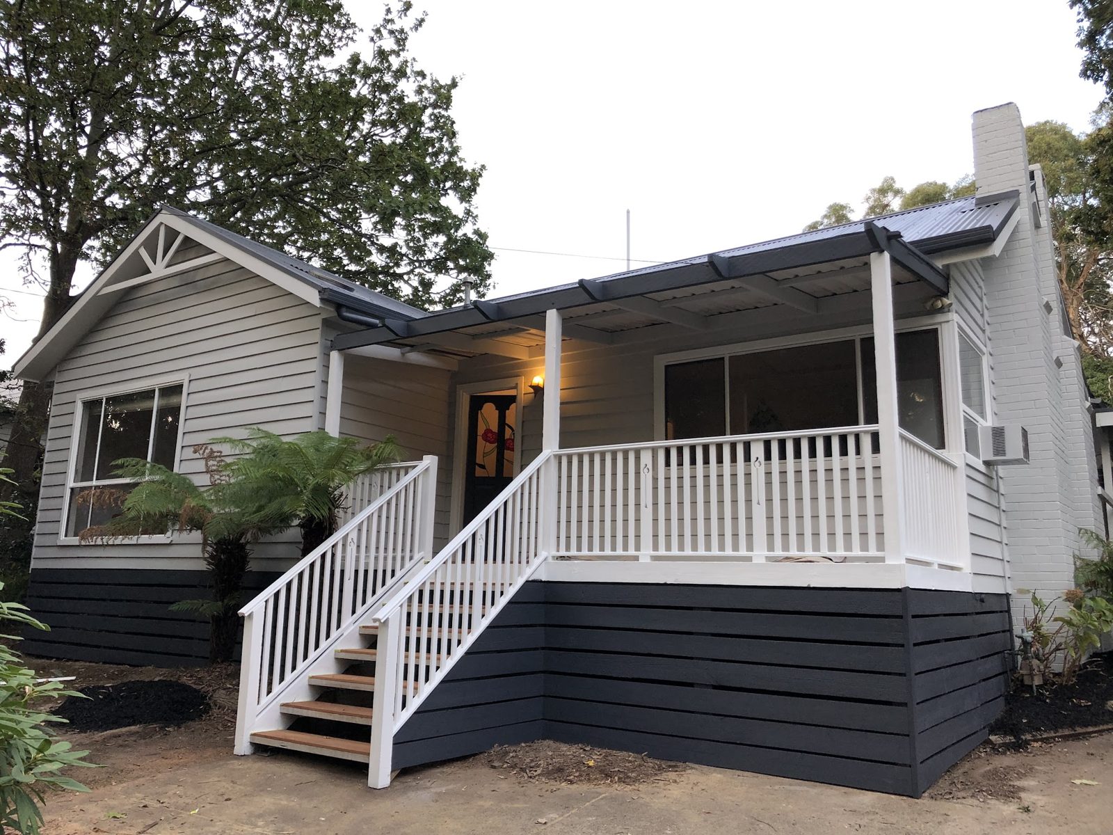Weatherboard bungalow repainted in pale grey with a charcoal base, white gable trim and new white front stairs