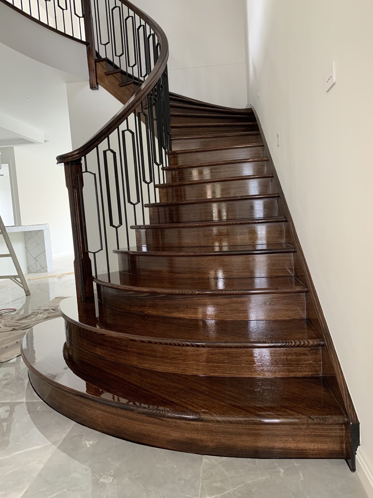 Curved timber staircase in a dark high-gloss finish with wrought-iron balusters